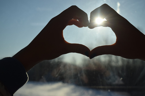 Hände bilden ein Herz durch das die Sonne scheint. 